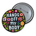 Glossy black pinback button with floral art and bold white text that reads “Hands Off My Body.” Feminist political button featuring bright pastel flowers in pink, red, orange, and yellow. Metal pin with durable safety pin back, shown in various settings: held by hand, displayed on pedestal, and against colorful street art. Available in 2" and 3" sizes, perfect for backpacks, jackets, tote bags, or as a gift for feminist allies and book lovers.